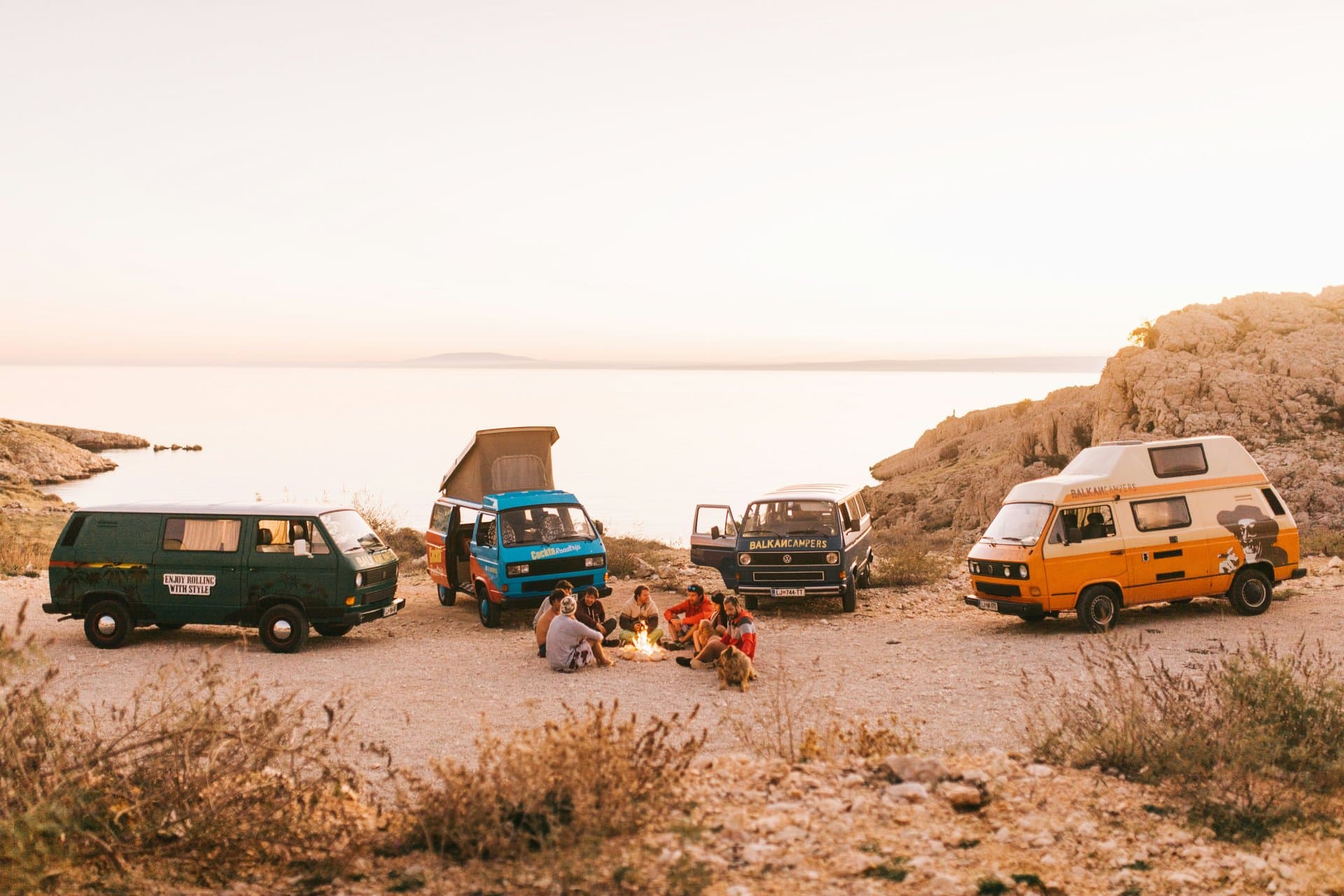 Groupe de vans réunis face à l'océan au coucher de soleil